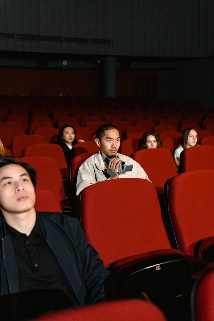 A small group of people watching a movie in an almost empty theater holding a camcorder.