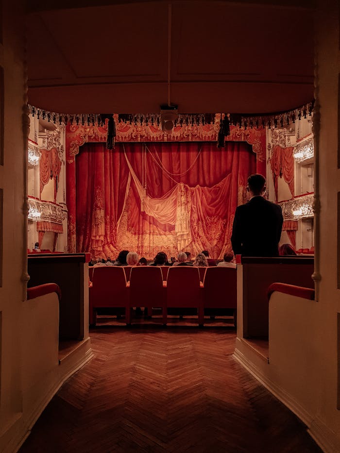 Elegant theater view with red velvet curtains and seated audience from an aisle perspective.