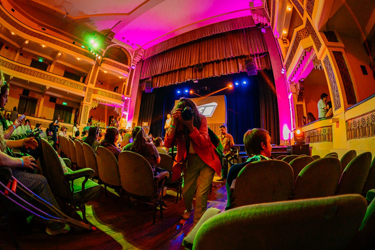 Capture of a lively theater event featuring a photographer in action amidst a crowd.